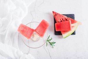 Wassermeloneneis am Stiel in einer Schüssel und ein Stück Wassermelone auf dem Tisch. hausgemachter Nachtisch. Ansicht von oben foto