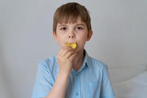 Konzept der Fettleibigkeit im Kindesalter. ein kleiner Junge im blauen Hemd auf grauem Hintergrund isst foto
