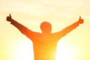 Ein Mann im Licht des Sonnenuntergangs mit erhobenen Händen, das Konzept von Erfolg, Freiheit und Freude foto
