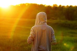 Ein Mann im Licht des Sonnenuntergangs mit erhobenen Händen, das Konzept von Erfolg, Freiheit und Freude foto