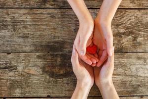 kleines rotes herz liegt in den händen von männern und frauen, das konzept von liebe und romantik foto