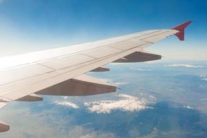 Flugzeugflügel auf den Wolken, fliegt auf dem Berghintergrund foto