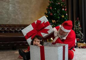 Kindermädchen, das in einer großen Geschenkbox sitzt, während es mit dem Weihnachtsmann spielt. Feiern Sie Feiertagsweihnachten und Erntedankfest. foto