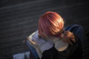 rosa Haare bei Mädchen. Mädchen zeichnet in Notizbuch. Student schreibt in Notizbuch auf der Straße. moderne Frisur. foto