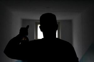 Silhouette eines Mannes mit einer Flasche Bier. Mann im Dunkeln zeigt Alkohol. Mann vor Türspion. unbekannte Person. foto