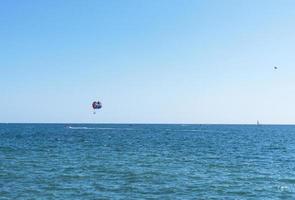 Parasailing mehrfarbiger Regenbogen Fallschirm hinter Boot über blau türkisfarbenem Meer Landschaft Sommeraktivitäten kopieren Raum selektiven Fokus foto