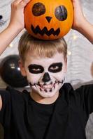 gruseliges Kind mit einem Make-up in Form eines Skeletts und mit einem Kürbis in seinen Händen foto