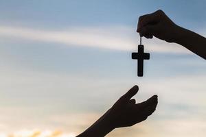 Silhouette aus Händen, die Holzkreuz auf Sonnenaufgangshintergrund, Kruzifix, Symbol des Glaubens halten. foto