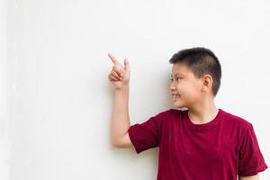 Lächelnder glücklicher asiatischer Junge, der mit dem Finger auf den Kopierraum zeigt, der über einem einfachen weißen Hintergrund isoliert ist foto