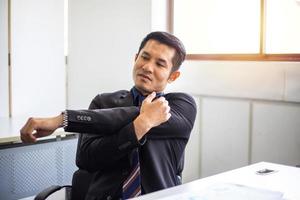 asiatischer geschäftsmann, der sich nach harter arbeit im büro dehnt, um schmerzen zu lindern. foto