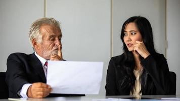 älterer geschäftsmann und geschäftsfrau sitzen in einer besprechung und überprüfen dokumente und notizbücher auf einem schreibtisch in einem besprechungsraum. foto