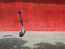 ein elektroroller, der in der sonne gegen eine rote wand geparkt ist foto