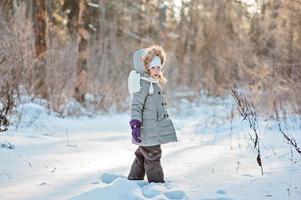 niedliches Kindermädchen, das im sonnigen Winterwald steht foto
