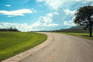 Panoramaszene der kurvenasphaltierten Straße auf dem Land am sonnigen Frühlingstag. Route in wunderschöner Naturlandschaft mit grünem Gras, Wolken und Sonne. kopierraum für reisende werbung. foto