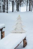 Vertikaler Schuss weißer künstlicher Tannenbaum auf einer mit Schnee bedeckten Bank, im frostigen Winterwald. Feiertagsdekoration. Saisonkonzept. Ferien. wunderbarer Winter foto