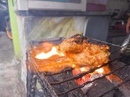 in knuspriges mehl gewickelte hähnchenbrust mit köstlichen würzigen gewürzen, gegrillt auf schwelender heißer holzkohle. ein typisches gegrilltes hähnchen aus indonesien foto