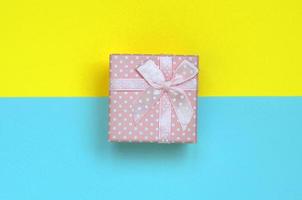 kleine rosa geschenkbox liegt auf texturhintergrund von modepastellblauem und gelbem papier in minimalem konzept foto