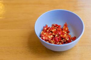 Gehackter roter Chili in eine blaue Tasse auf den Holztisch gelegt. foto