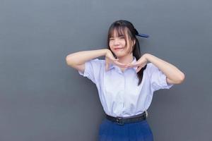 Schönes asiatisches Gymnasiastmädchen in der Schuluniform mit einem selbstbewussten Lächeln, während sie glücklich mit Grau im Hintergrund in die Kamera schaut. foto