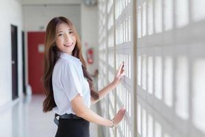 Porträt eines jungen thailändischen Studenten in Universitätsuniform. asiatisches intelligentes mädchen, das selbstbewusst mit ihrem glücklichen lächeln im schulgebäude steht foto