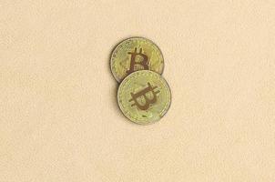 Zwei goldene Bitcoins liegen auf einer Decke aus weichem und flauschigem hellorangefarbenem Fleecestoff. physische Visualisierung der virtuellen Kryptowährung foto