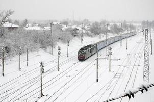 Ein langer Zug von Personenwagen bewegt sich entlang der Bahnstrecke. Eisenbahnlandschaft im Winter nach Schneefall foto