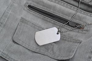 silberne Militärperlen mit Erkennungsmarke auf dunkelgrauer Weste mit Taschen foto