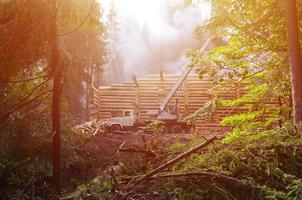 der Prozess des Baus eines Holzhauses aus Holzbalken mit zylindrischer Form. Kran in funktionstüchtigem Zustand foto