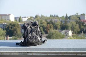 Der schwarze Rucksack liegt bei sonnigem Wetter auf dem Metallrand des Daches eines mehrstöckigen Wohngebäudes foto