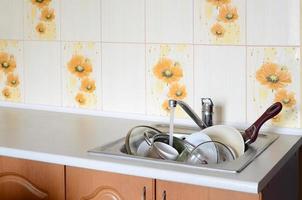 schmutziges geschirr und ungewaschene küchengeräte liegen in schaumwasser unter einem hahn eines küchenhahns foto