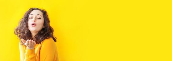 Liebe, Frieden. Schönheitsporträt junge glückliche positive Frau, die mit Kuss-Gesichtsausdruck posiert und Liebeszeichen auf gelbem Hintergrund isoliert zeigt. europäisches Mädchen. positive menschliche gefühle, banner foto