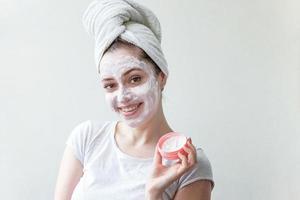 Schönheitsporträt einer Frau im Handtuch auf dem Kopf mit weißer pflegender Maske oder Creme im Gesicht, weißer Hintergrund isoliert. Hautpflege-Reinigung Öko-Bio-Kosmetik-Spa-Relax-Konzept. foto