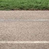 Textur gepflasterte Straße mit Markierungen auf dem Hintergrund des grünen Grases. ein Teil des Fotos ist verschwommen.