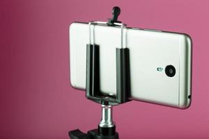 Smartphone auf einem Stativ als Foto-Videokamera auf rosa Hintergrund. Nehmen Sie Videos und Fotos für Ihr Blog auf.