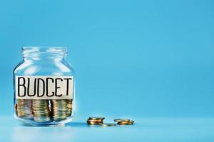 Ein Glasgefäß mit Münzen und einem Aufkleber mit der Aufschrift „Budget“ auf blauem Hintergrund. foto