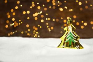 goldener weihnachtsbaum auf dem schnee mit neujahrslichtern von hinten. unscharfer Hintergrund. Weihnachtskarte foto