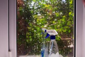 schmutziges fenster mit schaum benetzt mit einer flasche waschmittel. hinter Glas ein Baum mit grünen Blättern foto