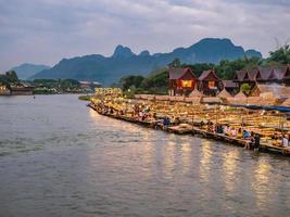 vangvieng.lao-11 dez 2017.schöne aussicht auf den nam song river mit touristen auf dem restaurant am flussufer und den berg in der nacht in vangvieng city lao.vangvieng city die berühmte urlaubszielstadt foto