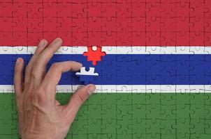 Die Gambia-Flagge ist auf einem Puzzle abgebildet, das die Hand des Mannes zum Falten vervollständigt foto