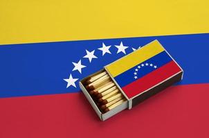 Die venezolanische Flagge wird in einer offenen Streichholzschachtel gezeigt, die mit Streichhölzern gefüllt ist und auf einer großen Flagge liegt foto
