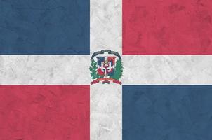 die flagge der dominikanischen republik ist in hellen farben auf der alten reliefputzwand dargestellt. strukturierte Fahne auf rauem Hintergrund foto