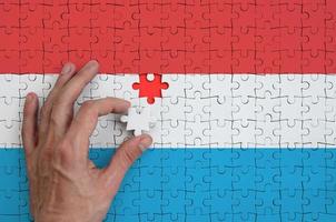 die luxemburgische flagge ist auf einem puzzle abgebildet, das die hand des mannes zu falten vervollständigt foto