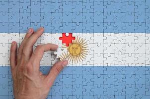 Die argentinische Flagge ist auf einem Puzzle abgebildet, das die Hand des Mannes zum Falten vervollständigt foto