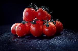 Reife rote Tomaten mit Wassertropfen auf der Haut auf dunklem Hintergrund. foto