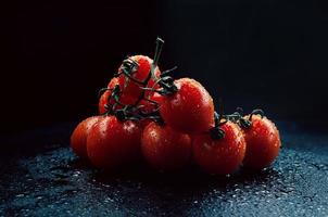 ein Zweig reifer Tomaten mit Wassertropfen auf dunklem Hintergrund. foto