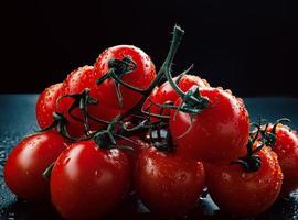 Reife rote Tomaten mit Wassertropfen auf der Haut auf dunklem Hintergrund. foto