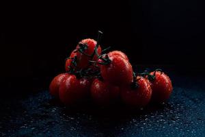 Zweig der reifen Tomaten auf dunklem Hintergrund. foto