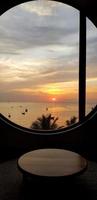 silhouette von tisch und fenster mit meer, himmel, kokospalme und sonnenuntergang oder sonnenaufgang im hintergrund am bangsaen beach chonburi, thailand. meerlandschaft mit sonnenlicht und landschaftsblick foto