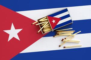 die kubanische flagge ist auf einer offenen streichholzschachtel abgebildet, aus der mehrere streichhölzer fallen und auf einer großen fahne liegt foto