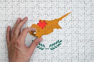 Die Flagge Zyperns ist auf einem Puzzle abgebildet, das die Hand des Mannes zum Falten vervollständigt foto
